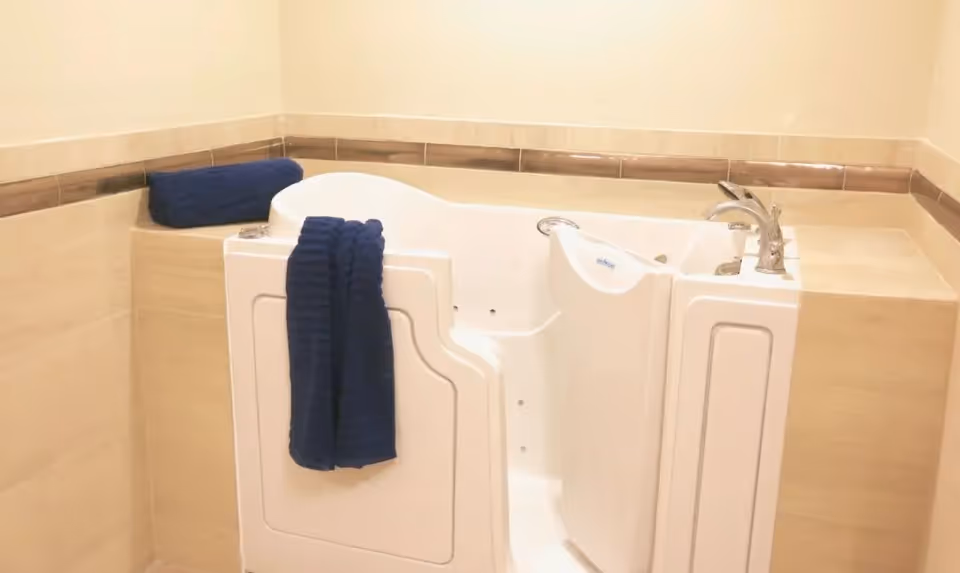 White walk-in bathtub with its door open and blue towels on a tiled ledge.