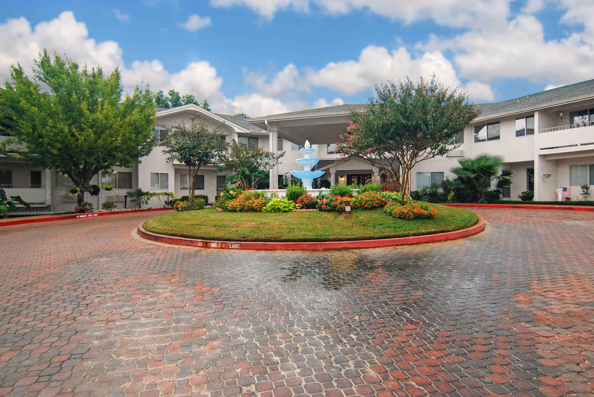 Two-story white senior living building with a circular driveway, central fountain and landscaped island.