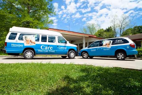 Two blue care vans are parked outside Colonial Nursing Home on a sunny day