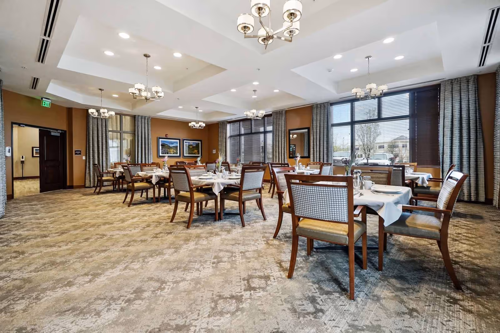 Spacious dining room with multiple set tables and chairs, chandeliers, and large windows.