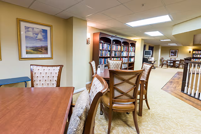 Well-lit interior common area with wooden tables and chairs and a bookshelf-lined wall.