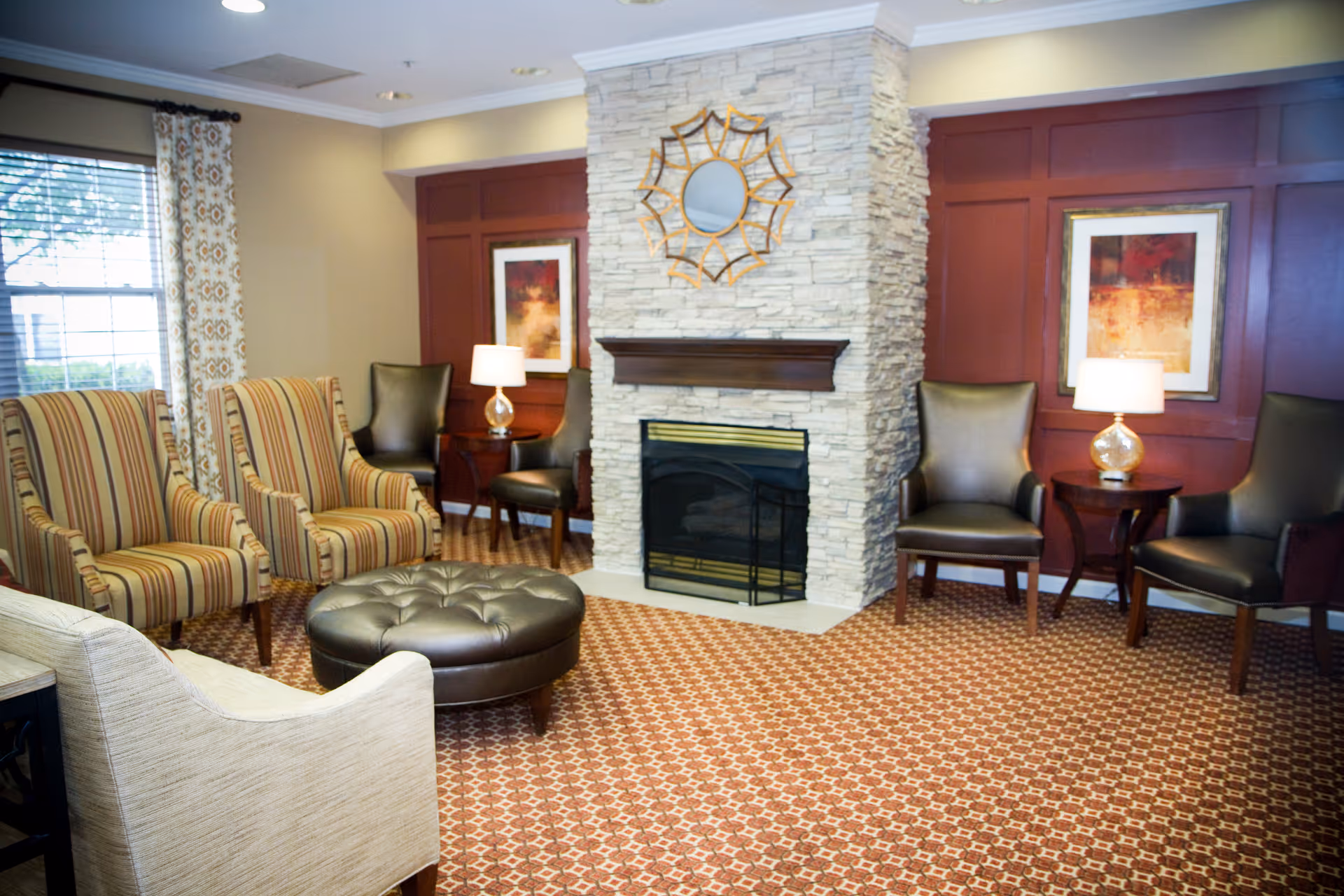 Cozy common sitting room with armchairs and a round ottoman arranged around a stone fireplace and decorative wall art.