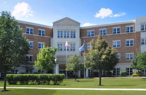 Greek American Rehabilitation & Care Centre building with lawn, trees, and flagpoles.