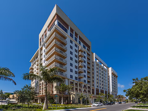 A modern multi-story Belmont Village Senior Living building with balconies along a sunny street.