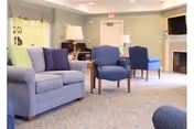 Well-lit lounge with sofas and upholstered armchairs arranged around side tables, a fireplace, lamps, and a wall-mounted TV.