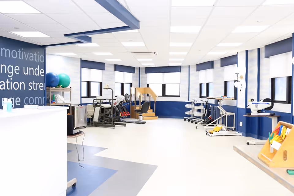 Bright physical therapy room with exercise equipment, therapy balls, parallel bars, and a small practice staircase.
