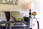 Gray sofa with patterned cushions, a glass coffee table holding a decorative bowl of bananas, and a side table with a lamp and flowers.