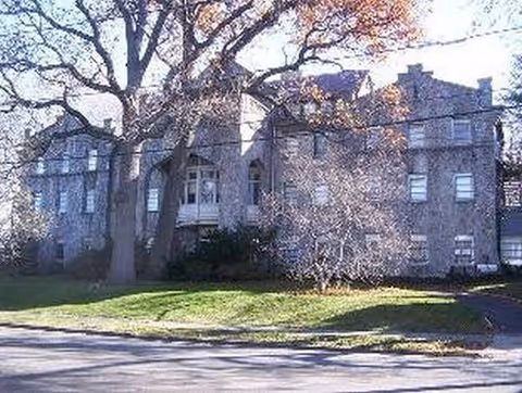 Front view of a stone senior living building with trees and a grassy lawn.