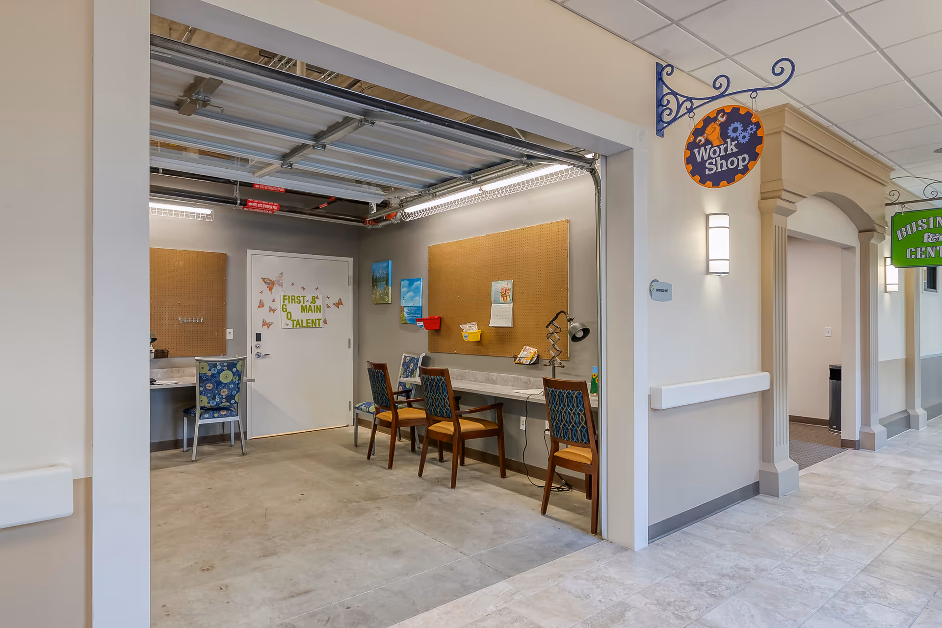 Interior view of a workshop/activity room with a long counter, chairs, pegboards, and a hanging 'Work Shop' sign.