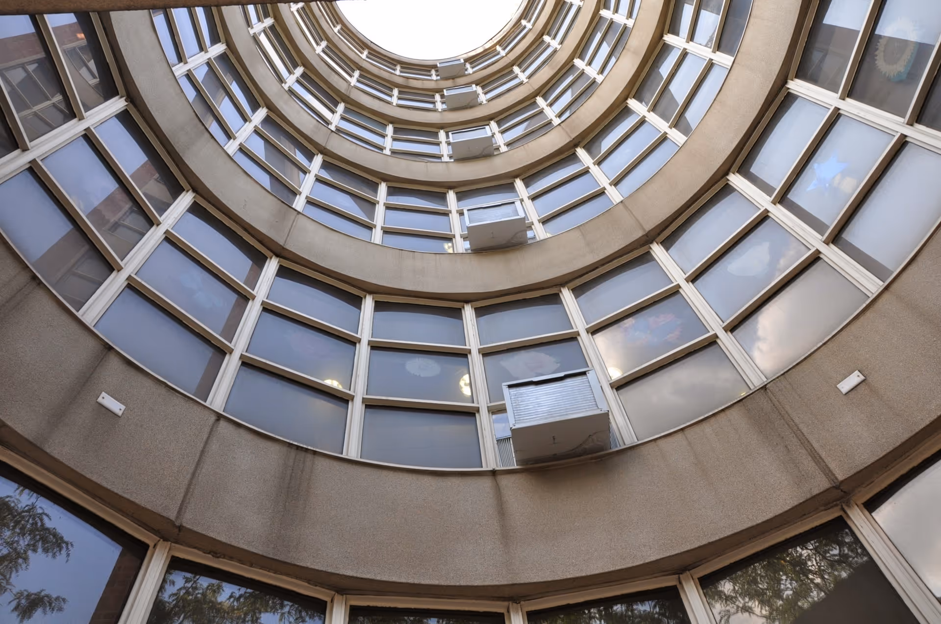 Upward view of the circular interior courtyard of a multi-story building with rows of windows and air conditioning units on each floor.