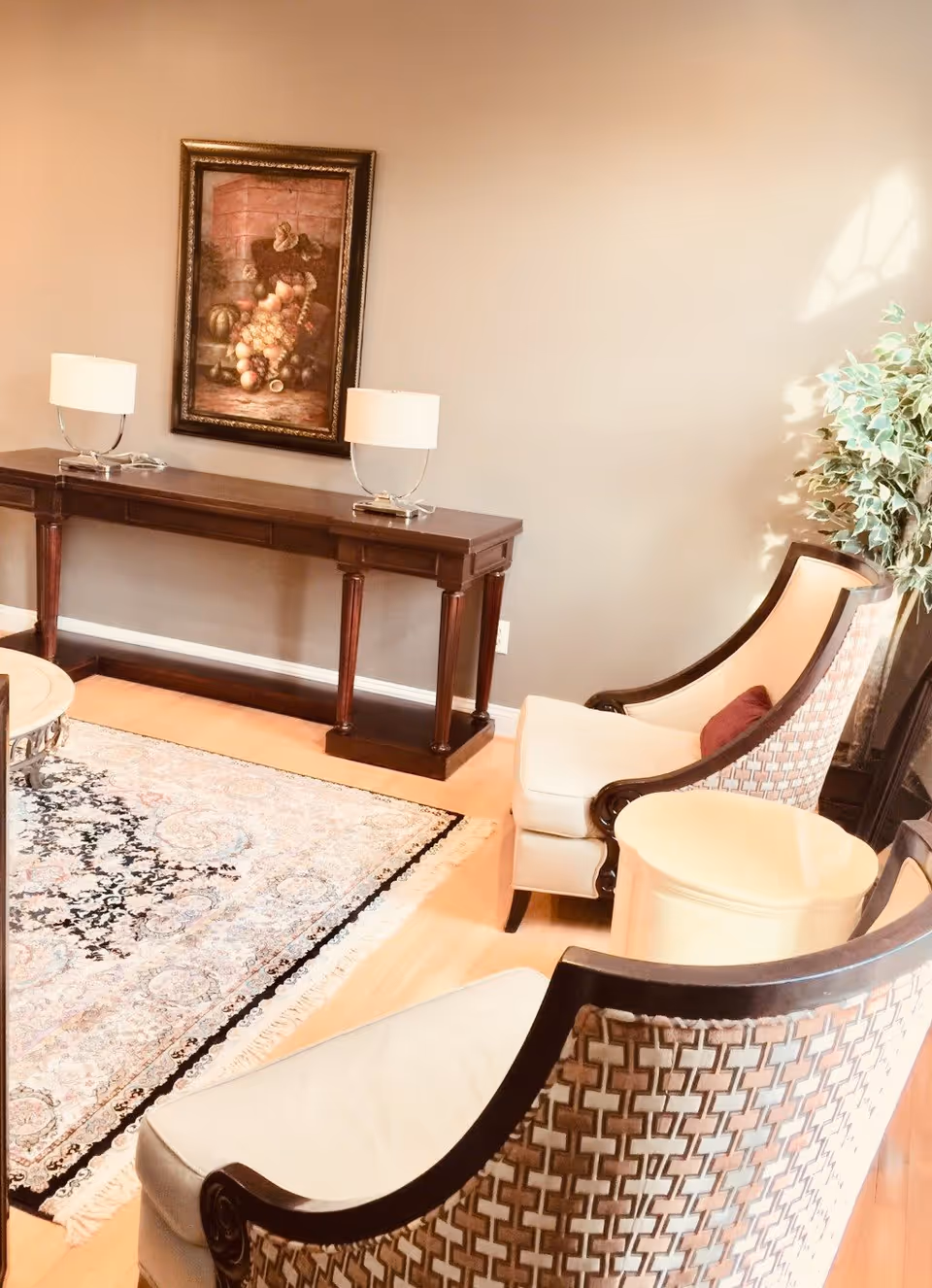 Cozy sitting area with two upholstered chairs, a patterned area rug, a dark wood console table topped with lamps and framed artwork on the wall.