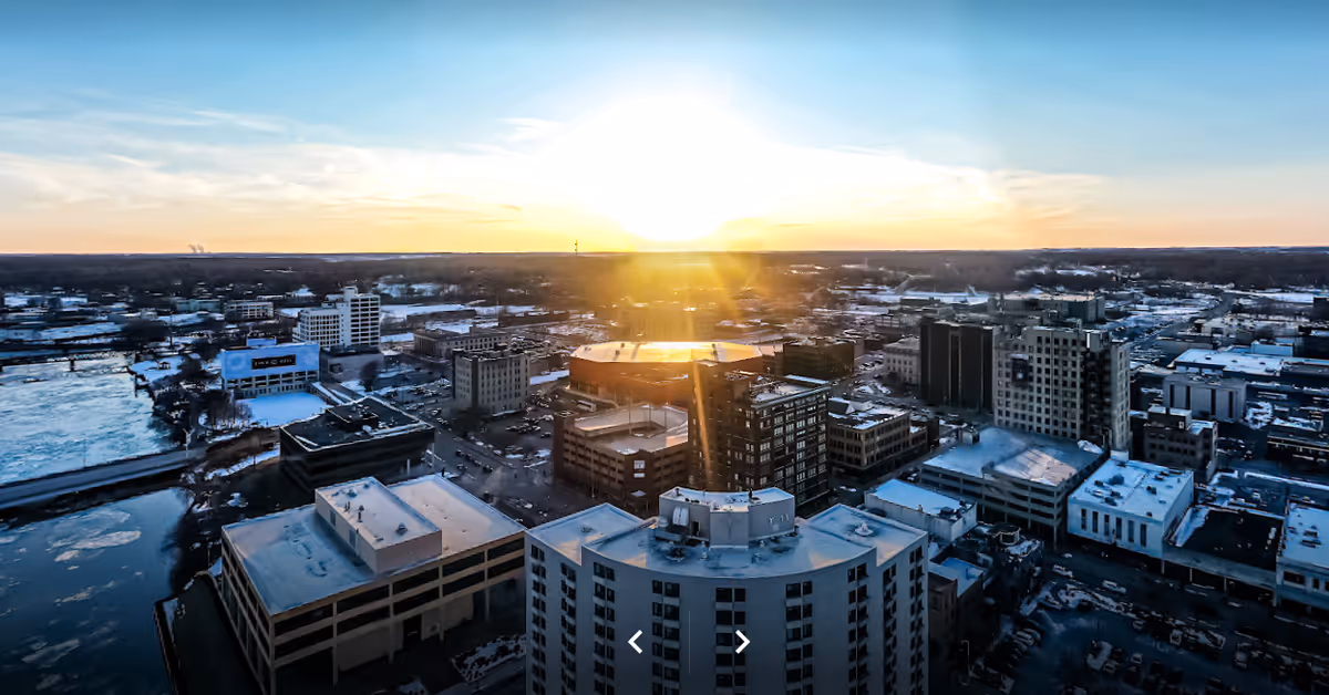 Aerial view of a downtown cityscape with snow-covered buildings and a river at sunset.