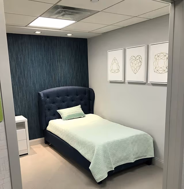 Small single bed with a tufted navy headboard, light green bedding, a nightstand, and framed geometric prints on the wall.