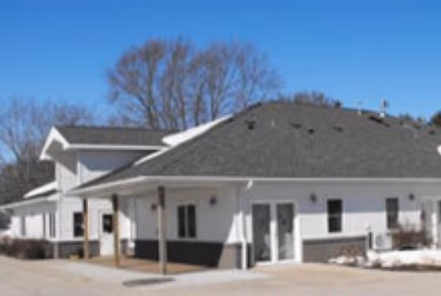 Front exterior of a single-story white assisted living building with a gray roof and driveway.