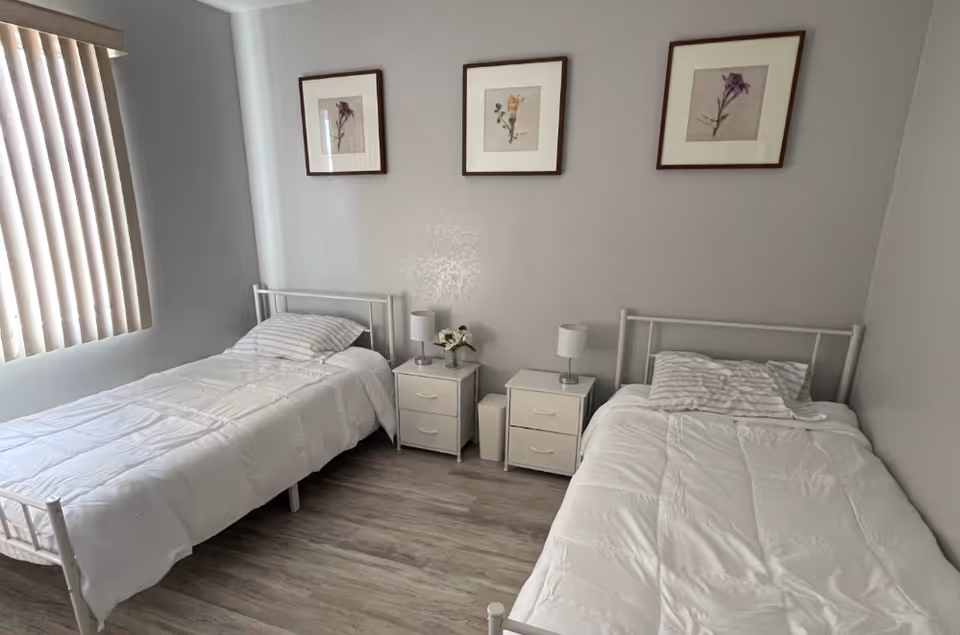 Two single beds with white bedding and nightstands in a light-filled bedroom.
