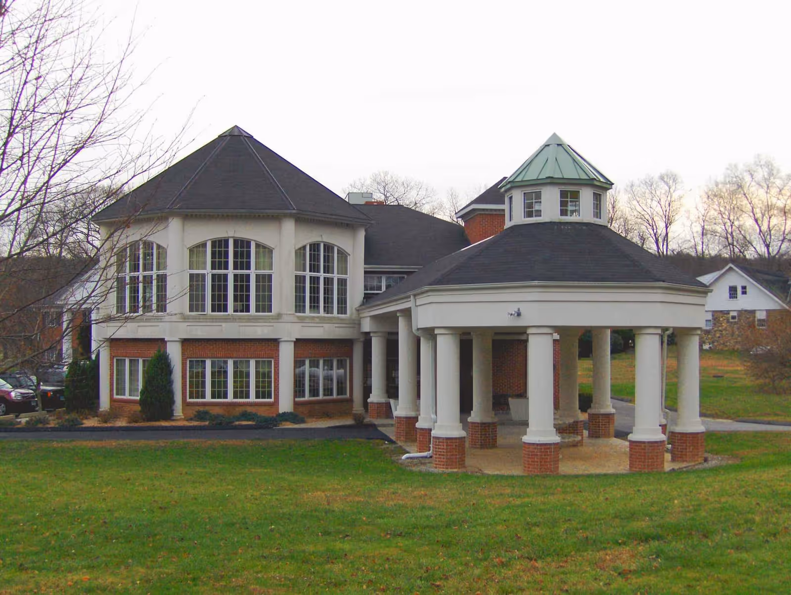 Front exterior of a two-story brick building with large arched windows and a columned circular porte-cochère on a grassy lawn.