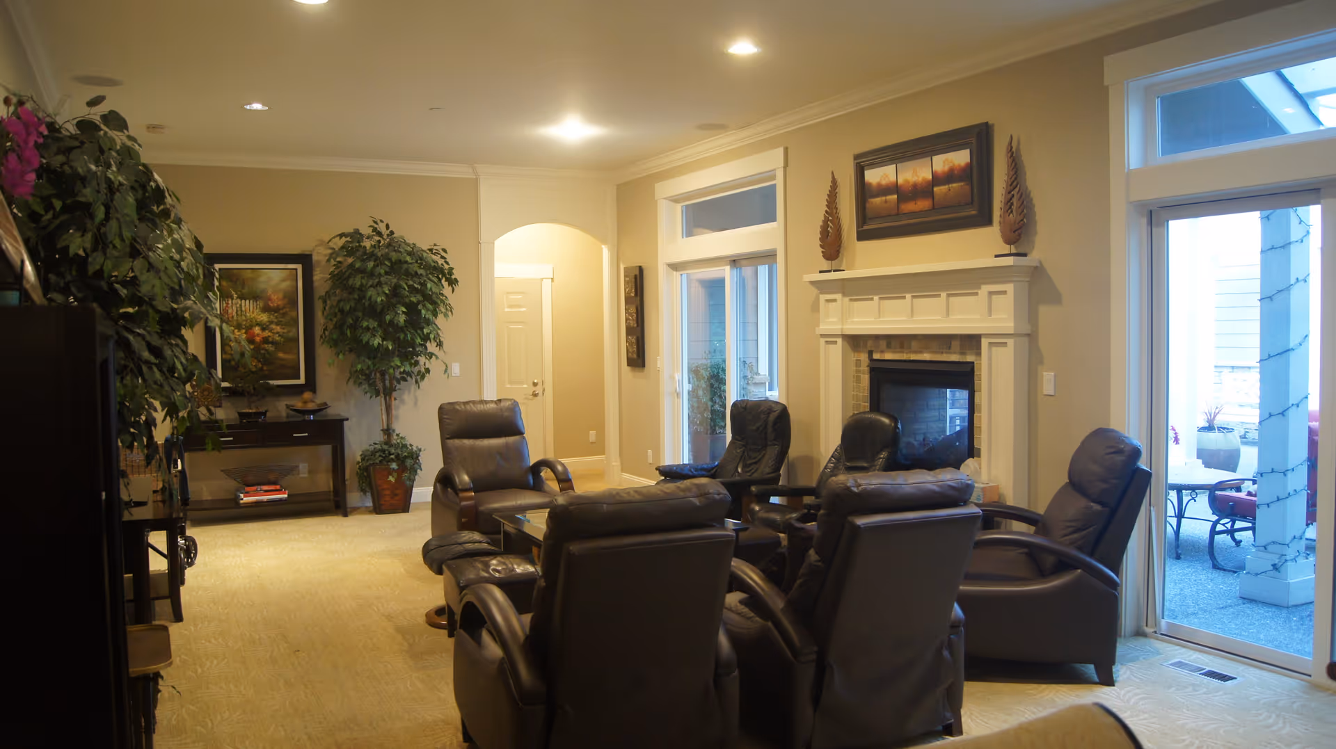 Spacious living room with multiple leather recliners arranged around a fireplace and large windows/doors opening to an outdoor patio.