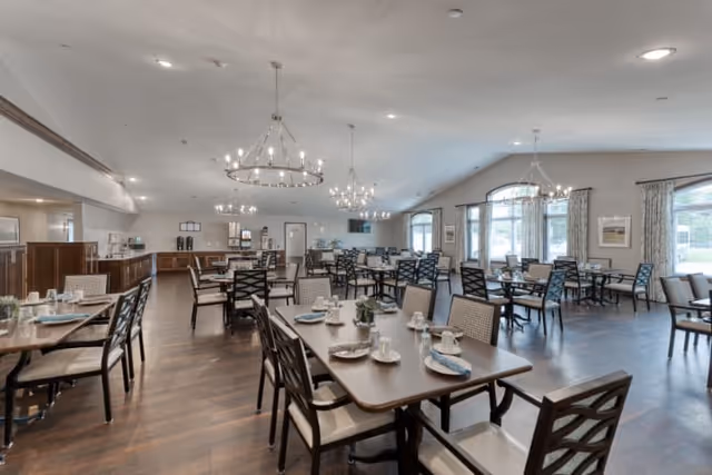 Spacious dining room with multiple set tables and chairs, chandeliers, large windows, and wood floors.