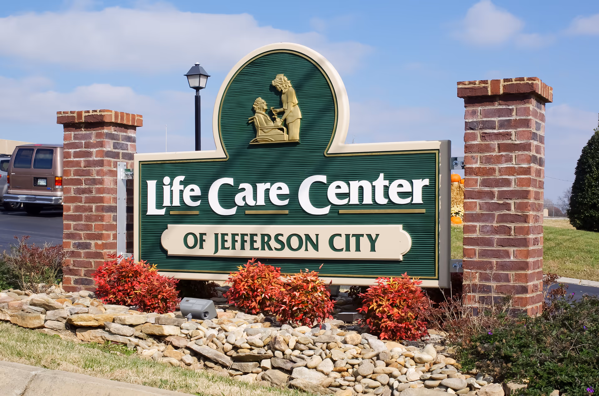 Entrance sign reading "Life Care Center of Jefferson City" mounted between brick pillars with landscaping and rocks.