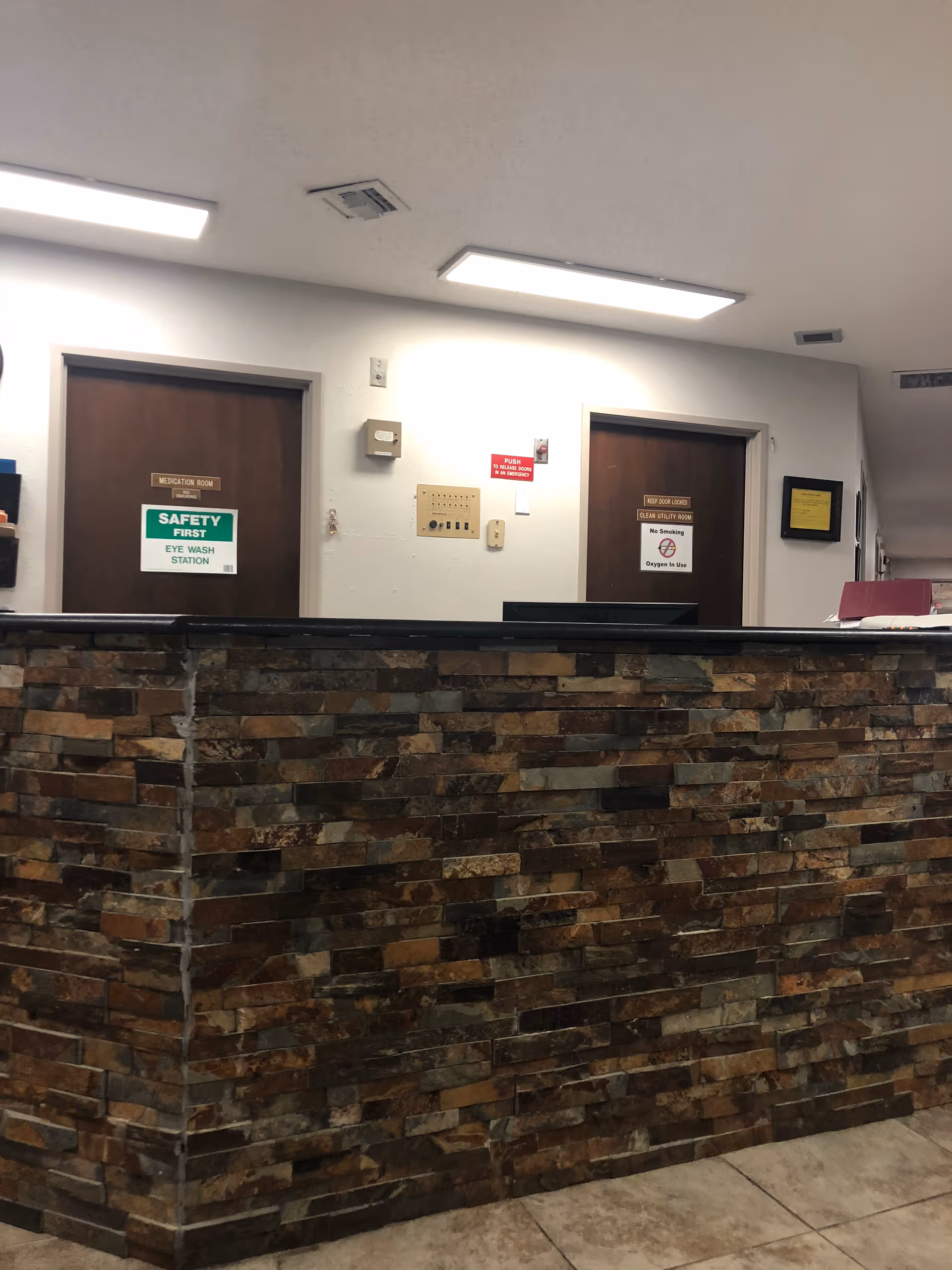 Reception desk with a stone-faced front and two closed doors and safety signs on the wall behind it.