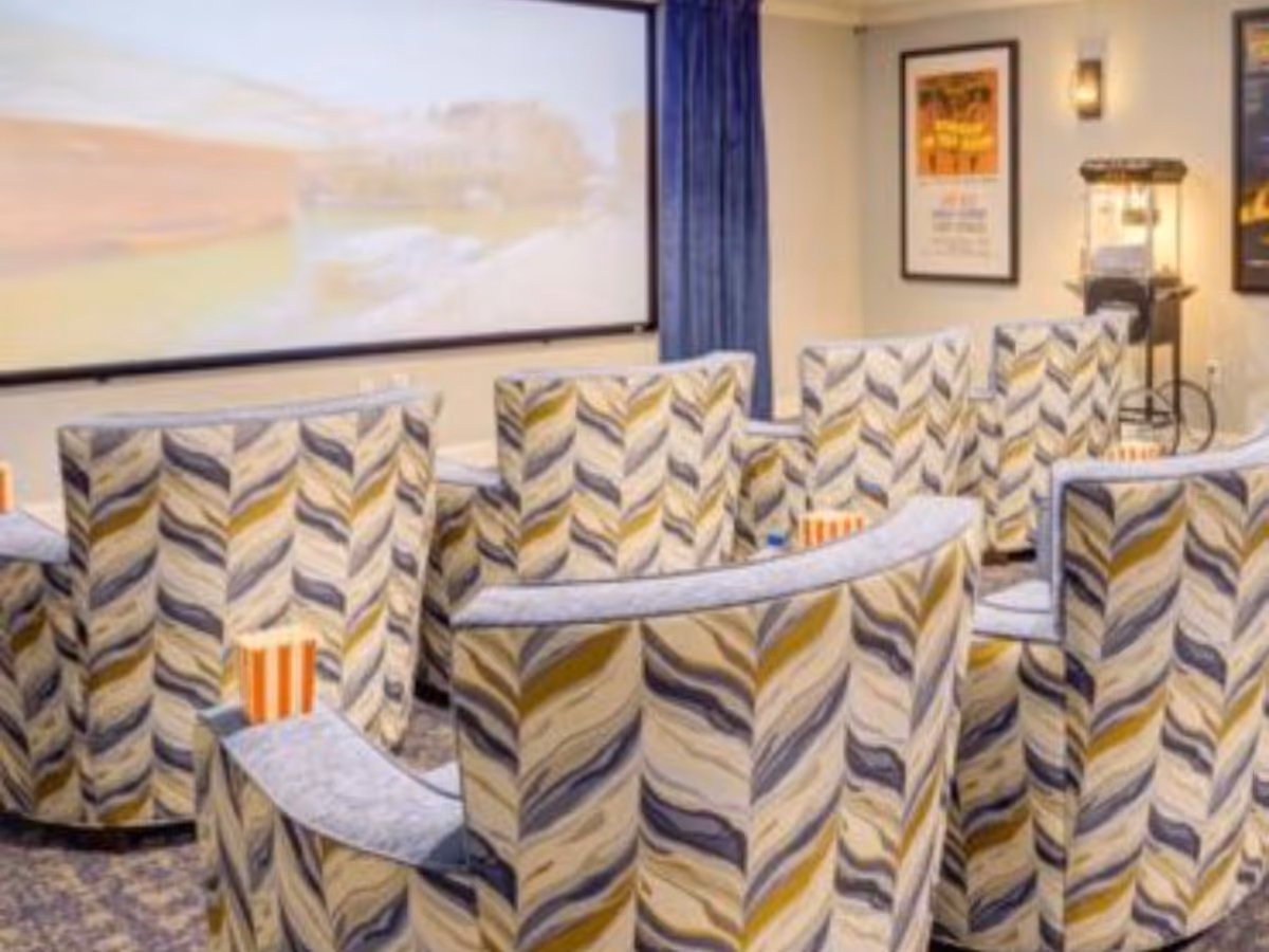 Small screening room with patterned upholstered theater chairs facing a large projection screen and a popcorn machine.