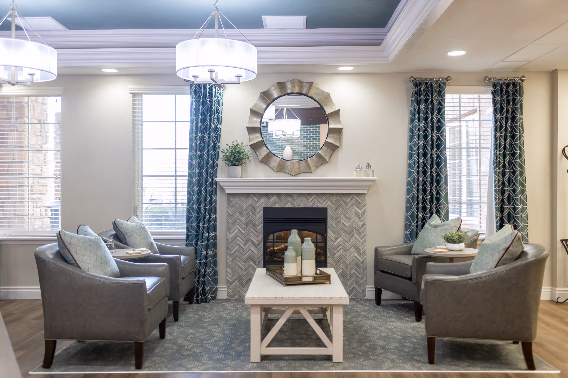 Cozy seating area with four armchairs arranged around a coffee table in front of a decorative fireplace and round mirror.