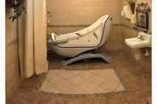 A bathroom with beige tiled walls and floor, featuring a specialized bathtub with a door for easy access, a white sink with a towel rack above it, and a shower curtain partially visible on the left side.