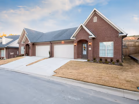 Front exterior of a single-story brick building with attached garages, driveways, and a manicured lawn.