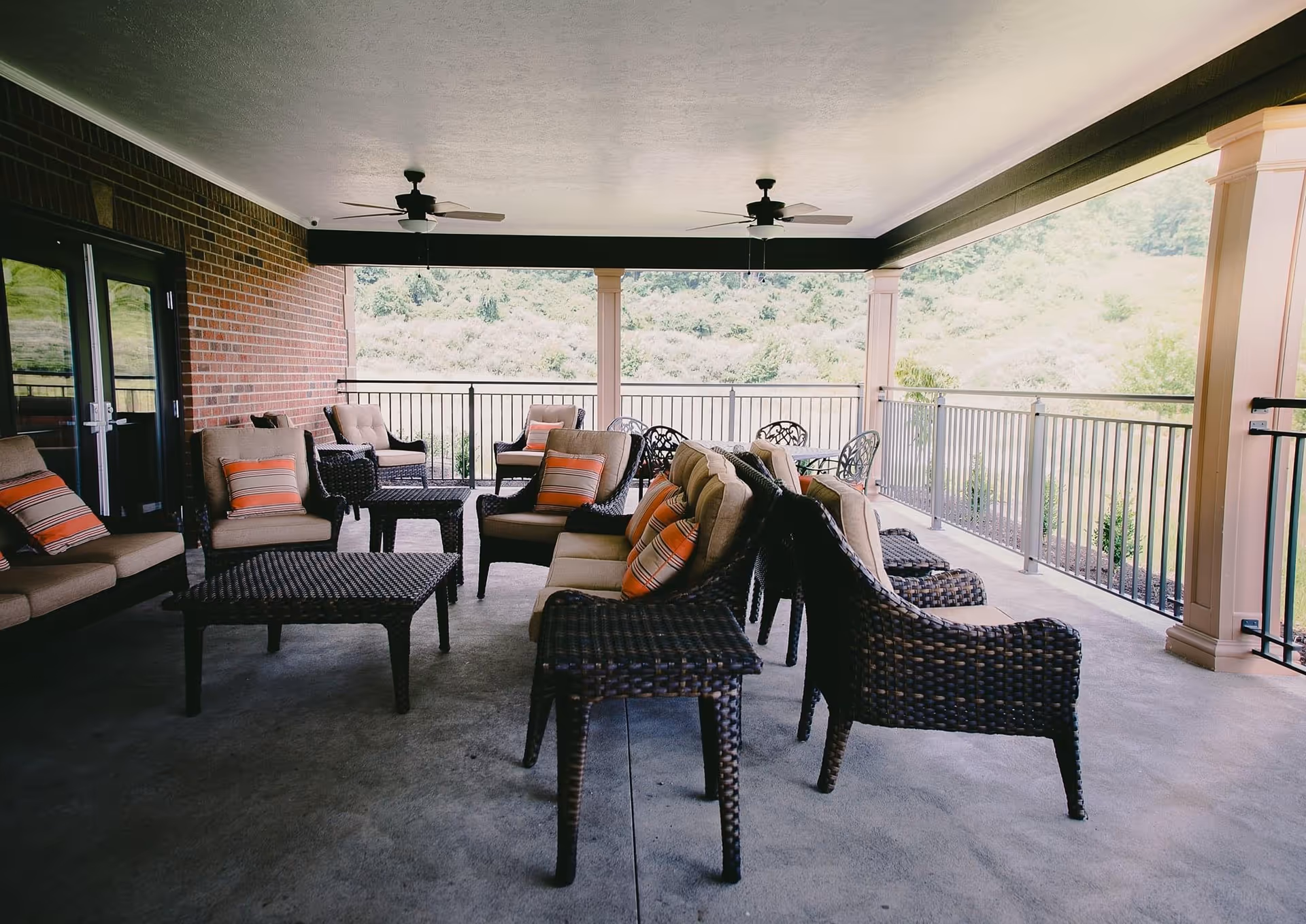 Covered outdoor patio with wicker chairs and sofas arranged around coffee tables overlooking greenery.