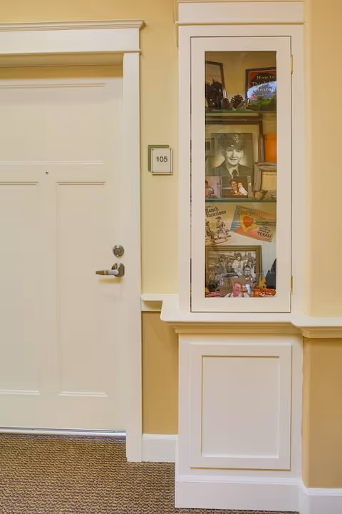 Hallway view of an apartment door labeled 105 next to a glass-front display cabinet containing framed photos and memorabilia.