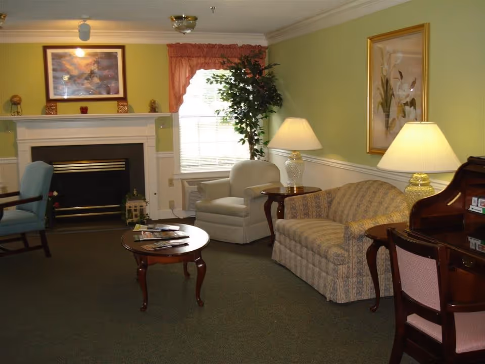 Cozy common living room with a fireplace, sofa and armchairs, coffee table, lamps, and framed artwork.