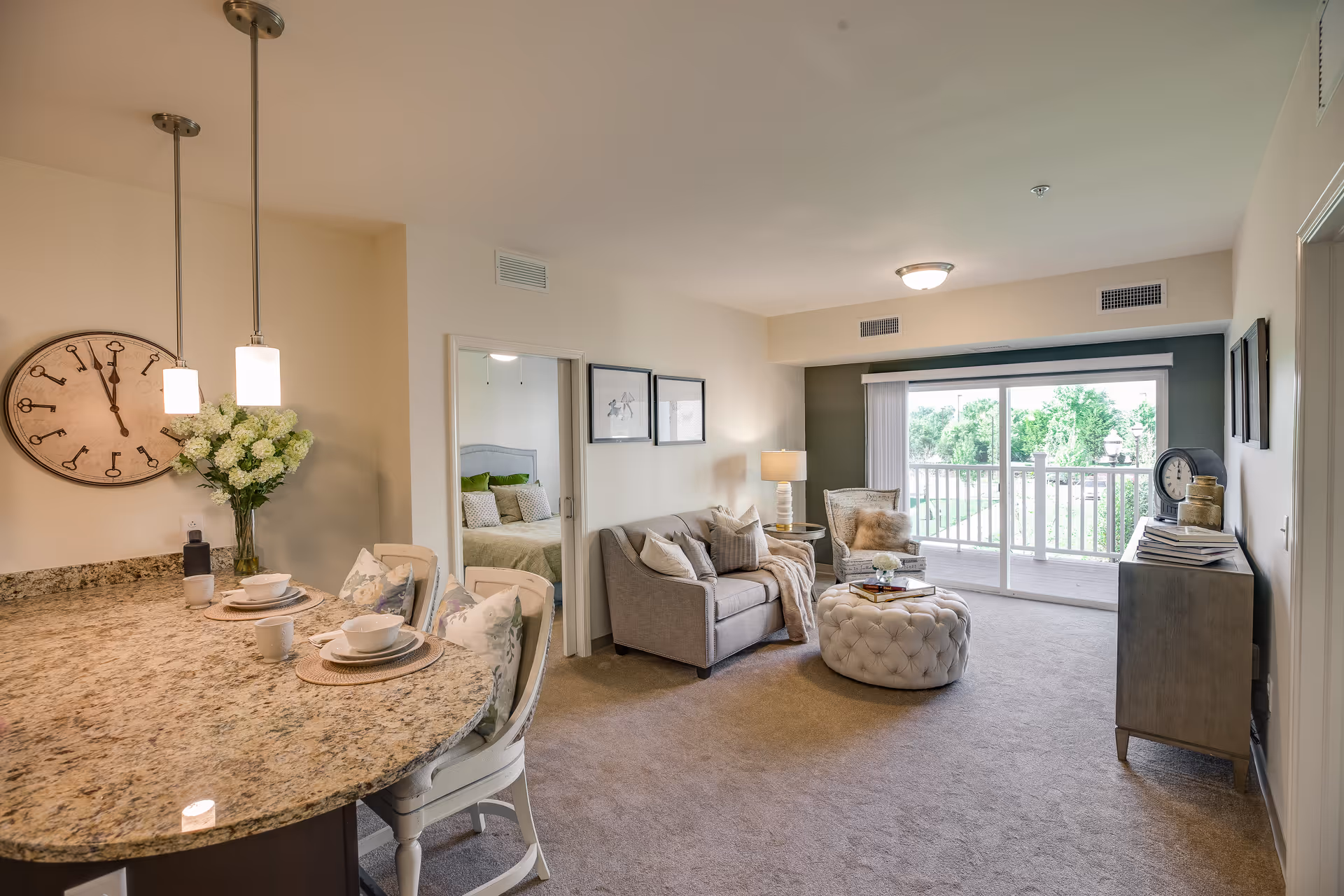 Bright open-plan living area featuring a granite breakfast bar with place settings, a sofa and tufted ottoman, and sliding glass doors to a balcony.