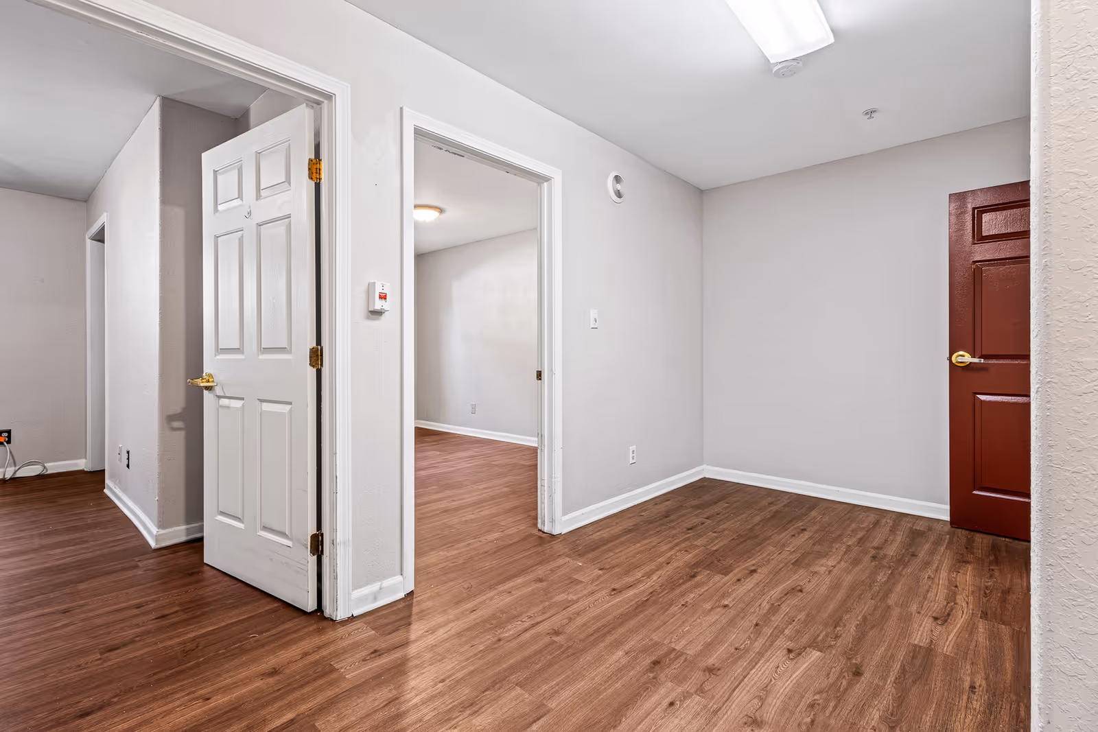 Empty interior space with wood laminate flooring, white and red doors, and open doorways to adjacent rooms.