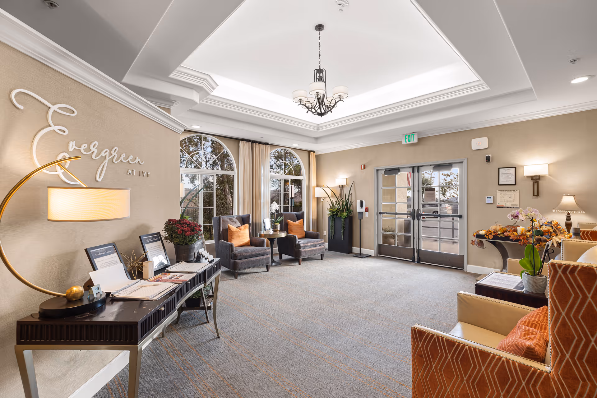 Bright, furnished senior living lobby with armchairs, side tables, decorative lamps and double glass entrance doors.
