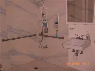 Accessible bathroom with grab bars, wall-mounted sink, and shower fixtures.