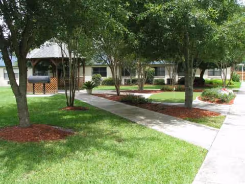 Well-kept lawn and trees line a sidewalk leading to the front of a low-rise senior facility.