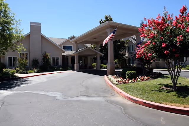 A sunny exterior view of Marbella Chico senior living facility with flowers and American flags.