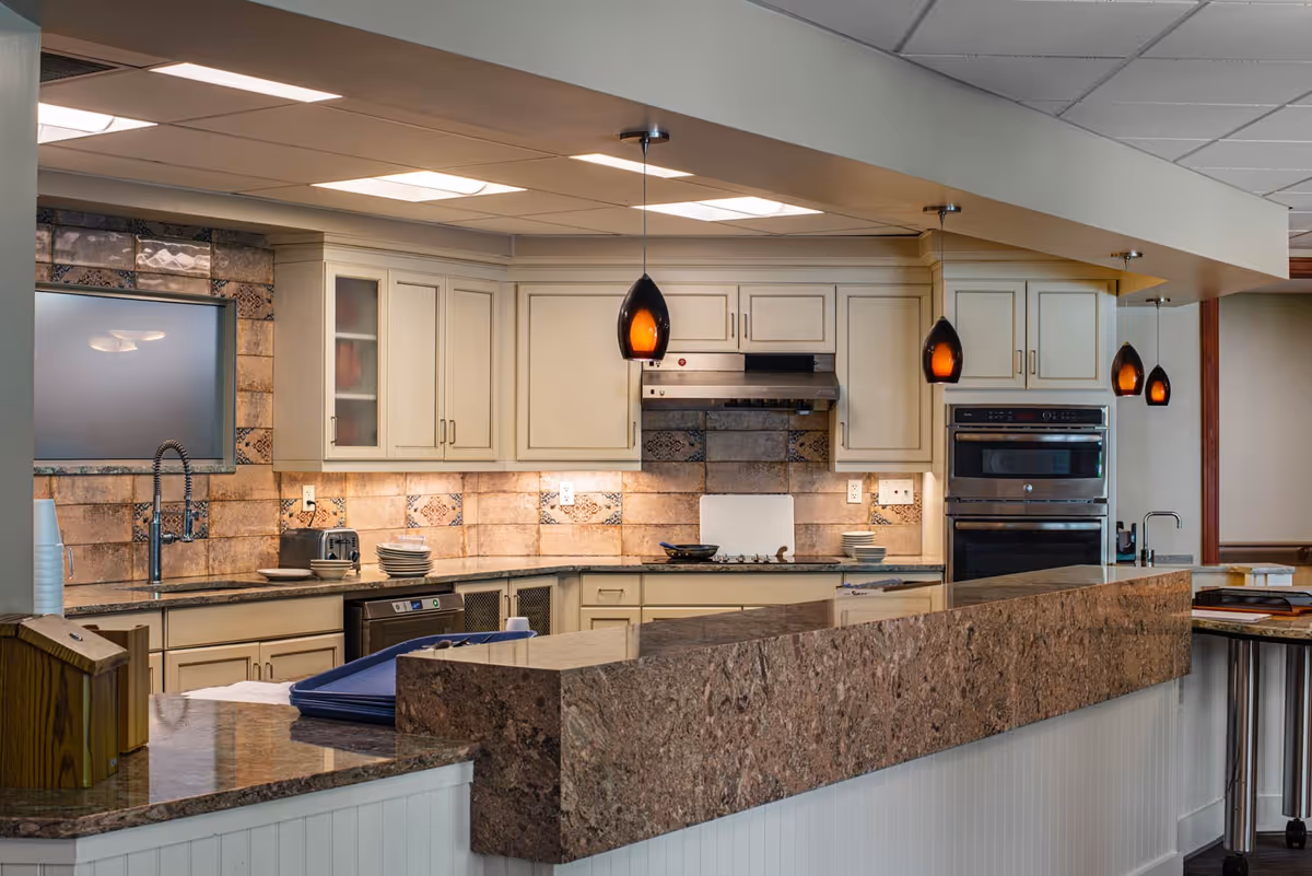 Communal kitchen area with marble countertops, cream cabinets, stainless appliances, and pendant lighting.