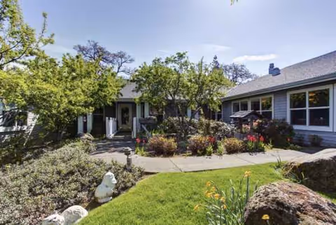 Single-story senior living facility with entrance, lush landscaping, and a curved walkway.
