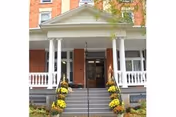 Front entrance of a brick building with white columns and a porch decorated with yellow flowers on both sides of the stairs leading up to the door.