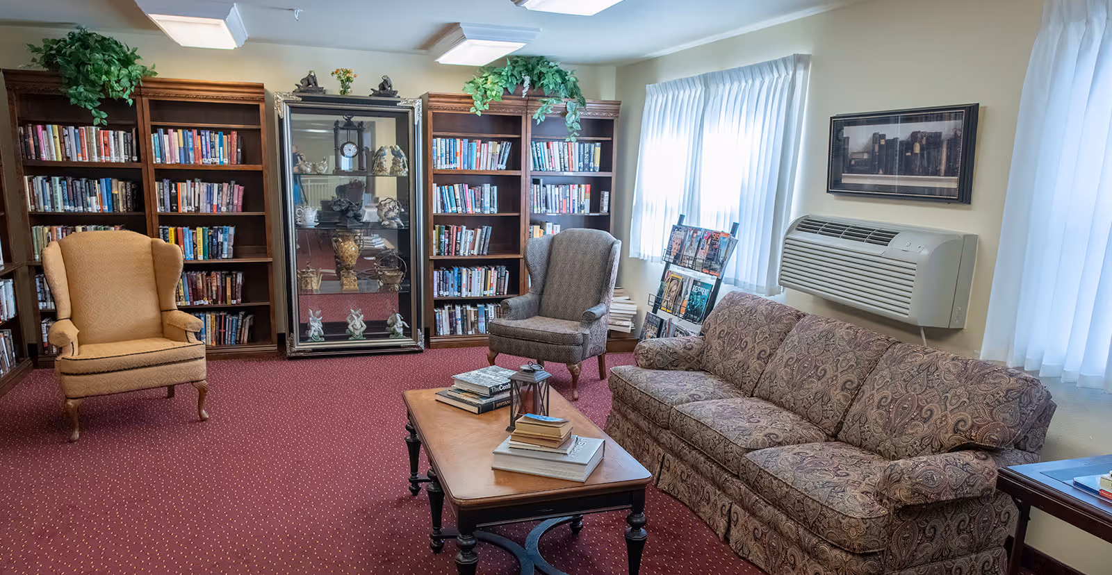 Cozy common room with bookshelves, armchairs, a sofa, coffee table and a display cabinet.