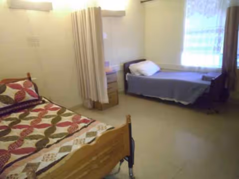 Two beds and a dresser in a small, shared senior living bedroom.