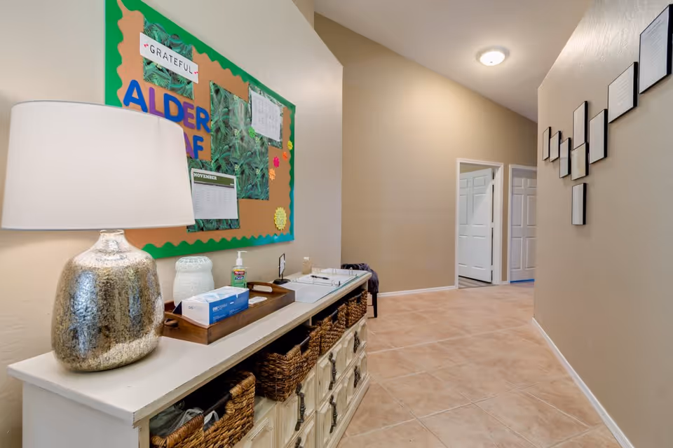 Interior hallway with a console table holding a lamp and wicker baskets and a bulletin board labeled "ALDER" on the wall.
