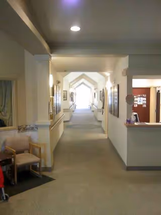 Long, bright interior hallway in a senior living facility with seating and a reception desk.