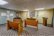 Small chapel-style interior with wooden pews facing a pulpit, framed artwork, and wall-mounted sconces.