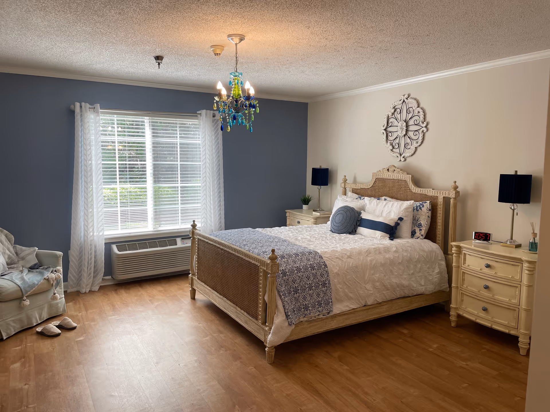 Spacious bedroom with a carved bed, matching nightstands, blue accent wall, and chandelier.