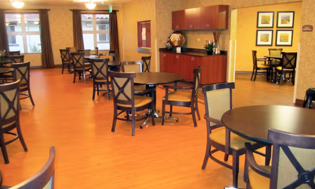 Dining room with multiple round tables and chairs on a wood floor, cabinets and framed art on the walls.