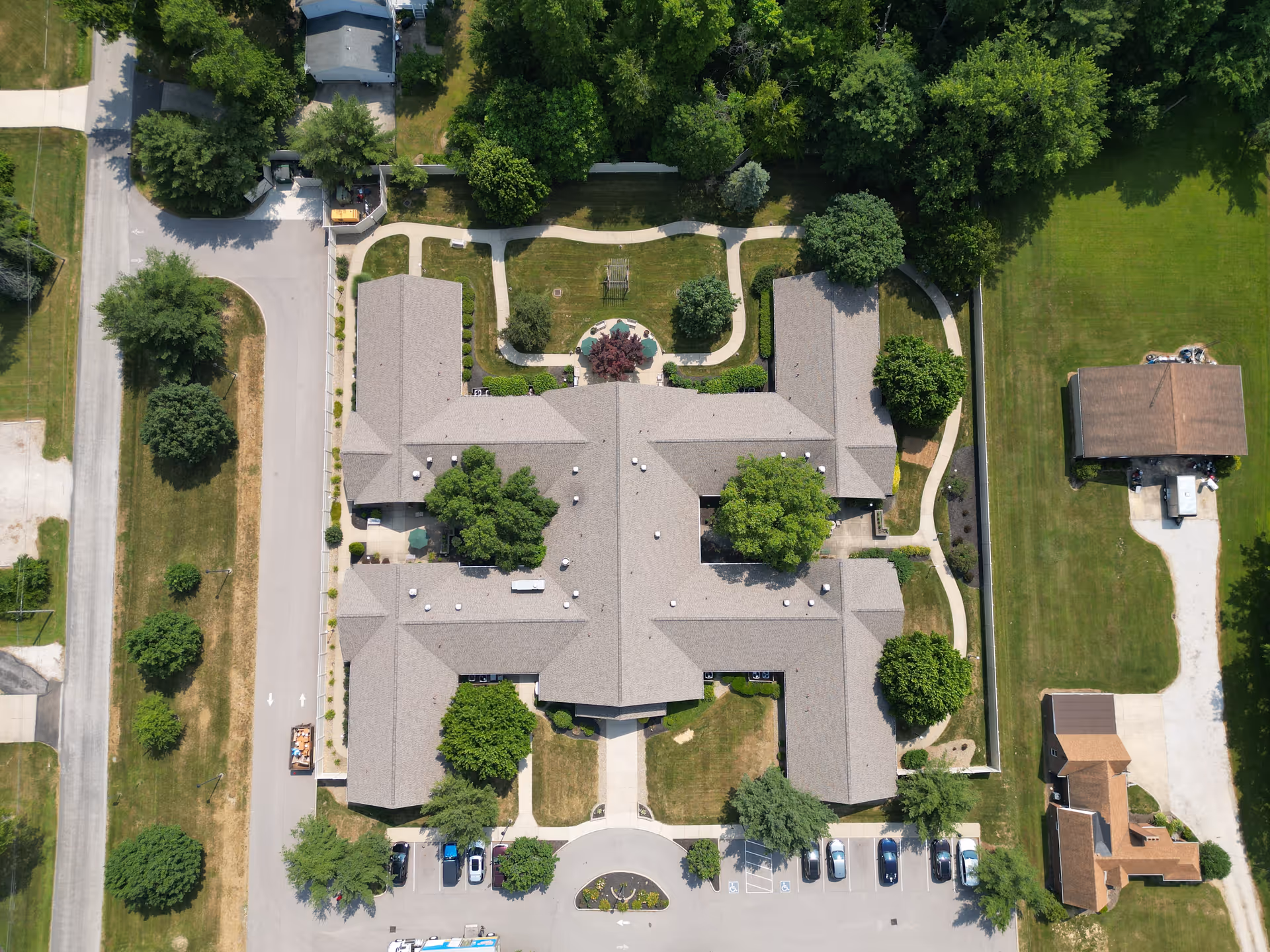 Aerial view of a memory care facility showing the building roof, surrounding parking, walkways, lawns and trees.