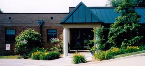 Front exterior of The Harmar Place Community with brick facade, green roof, and landscaped entrance.