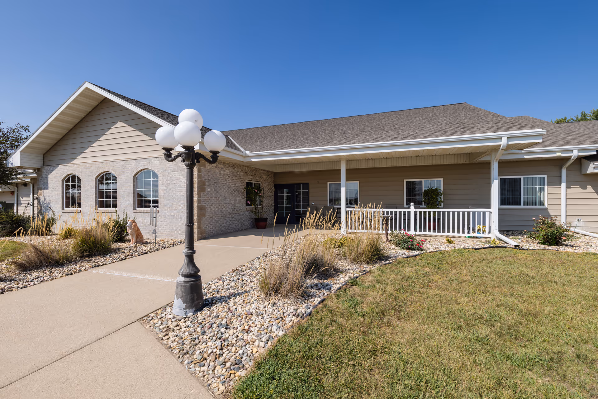 Single-story senior living building front with a covered entrance, walkway, lamp post, and landscaped gravel beds.